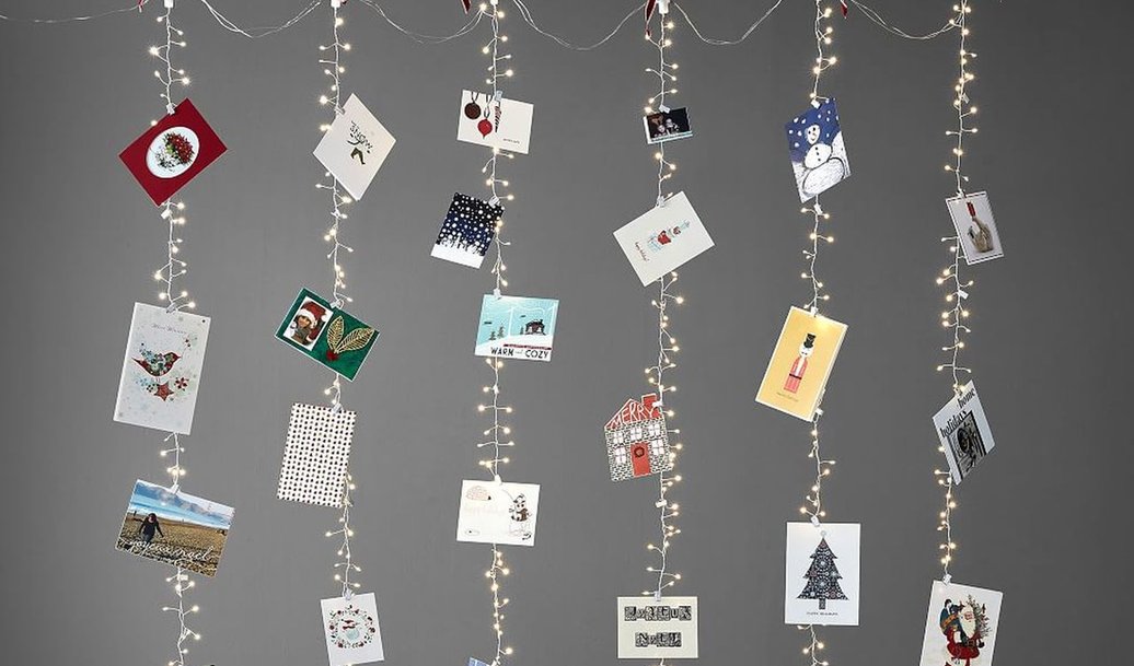 Floor-to-ceiling curtain string lights suspended behind sheer linen drapes displaying festive holiday greeting cards