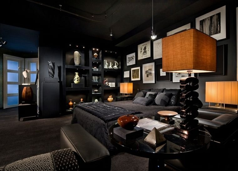 Dark bedroom featuring black floating shelves, bronze sculptures, and matching table lamps with amber bulbs.