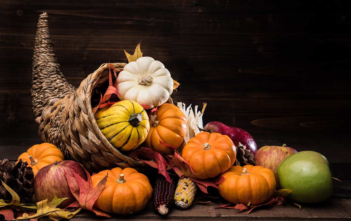 Evening dining room, dark wooden table, orange pumpkin cornucopia, red apple, soft candlelight.