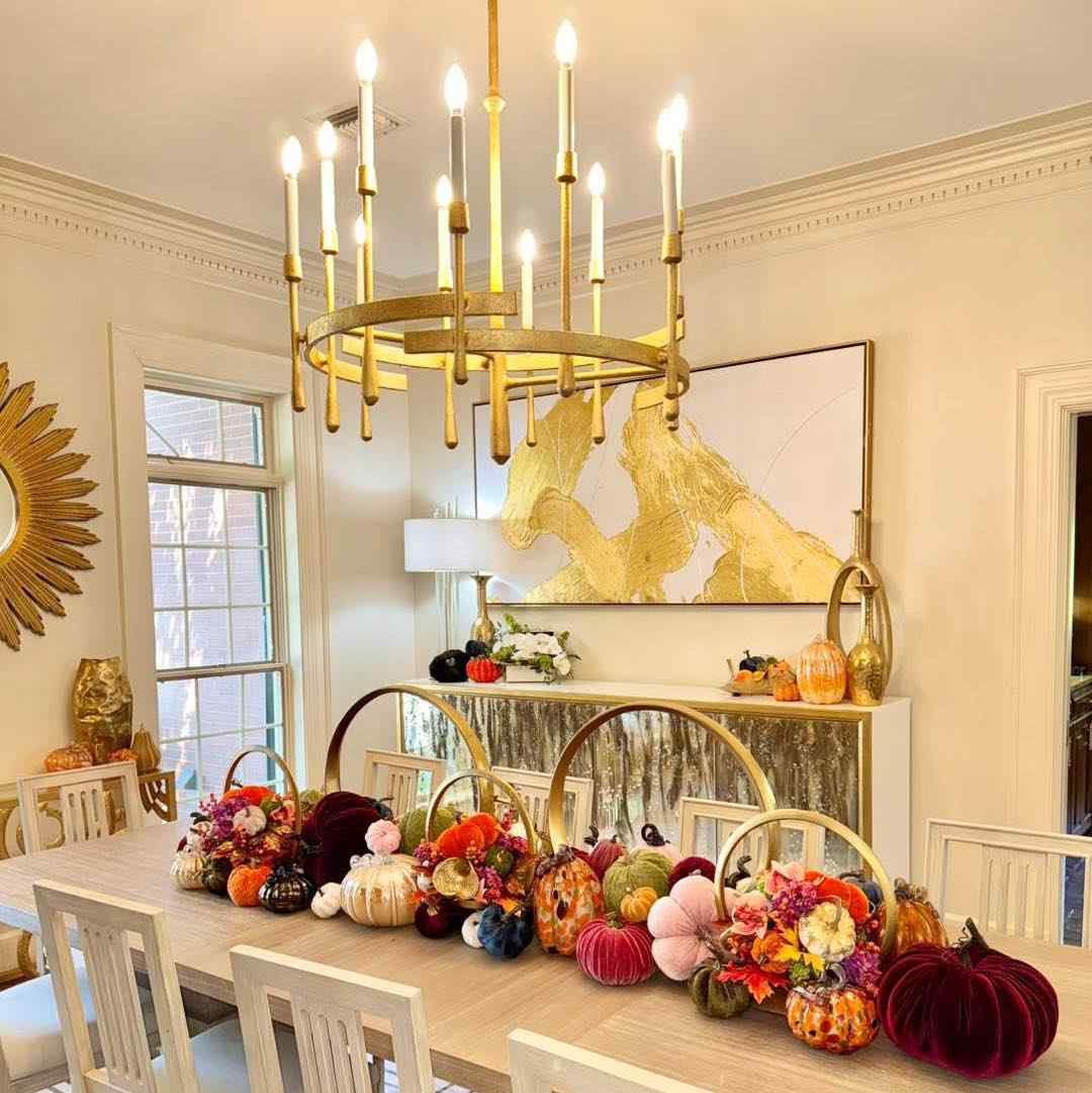 Dining room, velvet upholstered chairs, pumpkins, gold ring vases, soft low lighting, dark wood table.