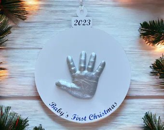 Cozy farmhouse living room shelf displaying a natural wood slice ornament with painted baby handprint, pinecones, and warm candle glow.