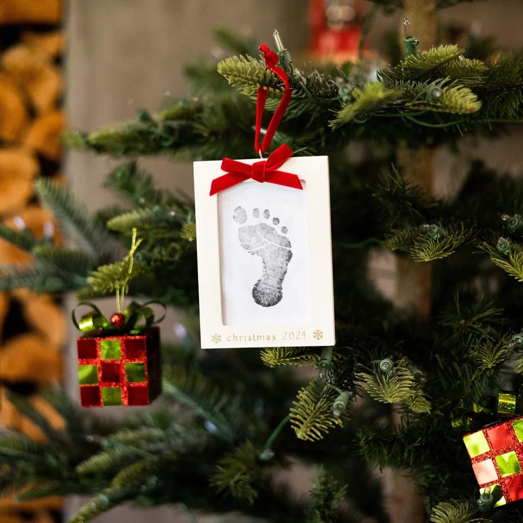 Rustic stone fireplace hearth with live-edge wood slice baby handprint ornament, plaid throw, warm firelight.
