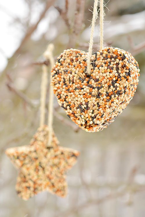 Small rustic burlap pocket ornament stuffed with birdseed and evergreen sprigs hanging on a fence.