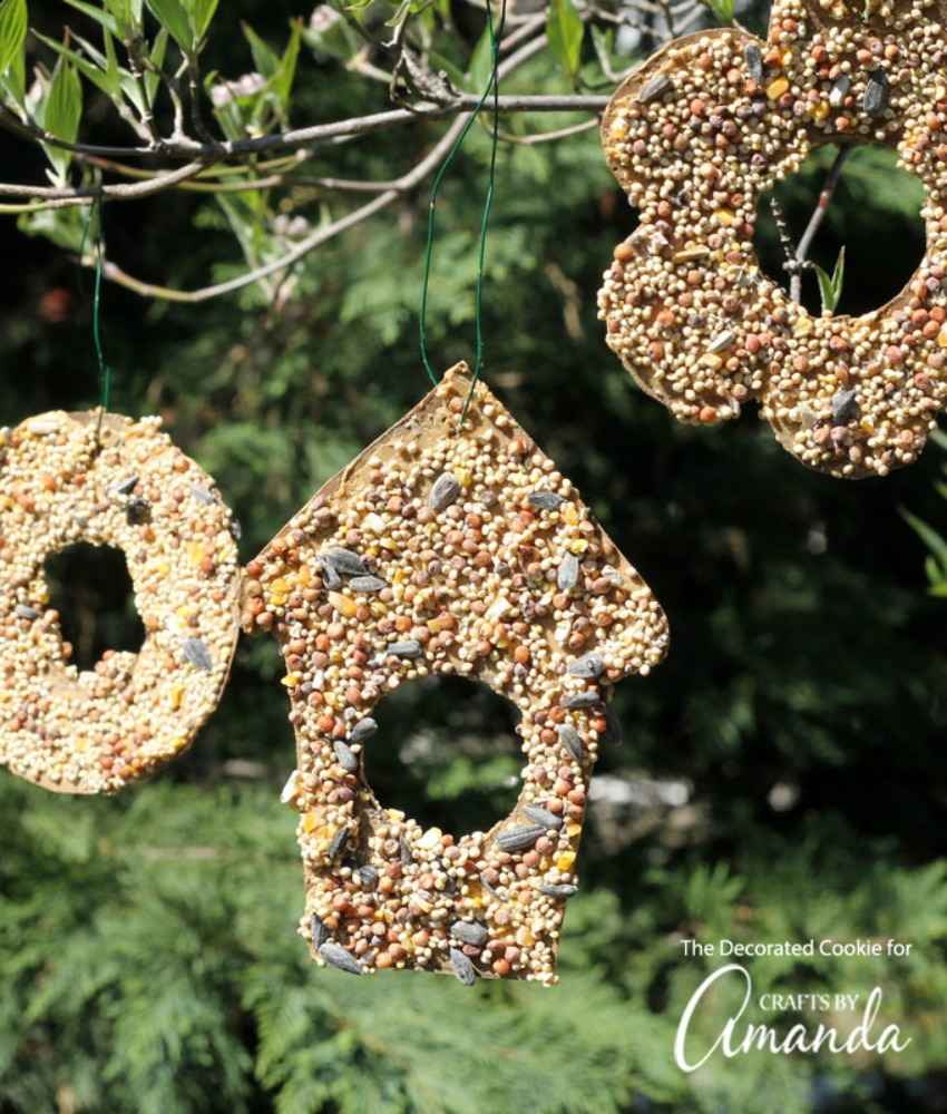 Sunlit kitchen window frame featuring wooden garland, hanging birdseed bells, light oak trim, soft morning sunlight.