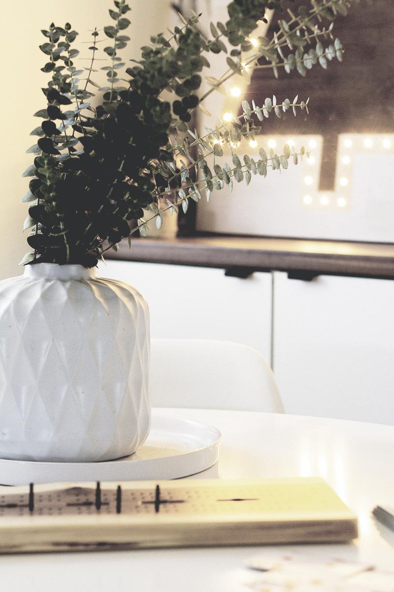 Entryway console with a metal JOY marquee sign glowing brightly beside textured boucle pillows and eucalyptus.
