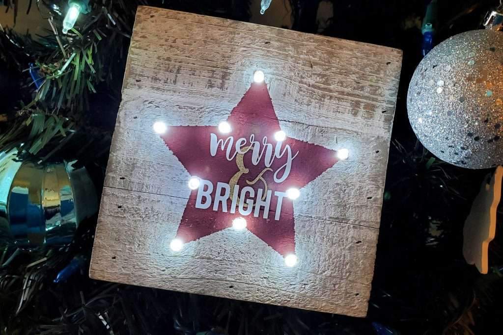 Rustic living room fireplace mantel featuring a silver metal snowflake marquee light and pine garland.