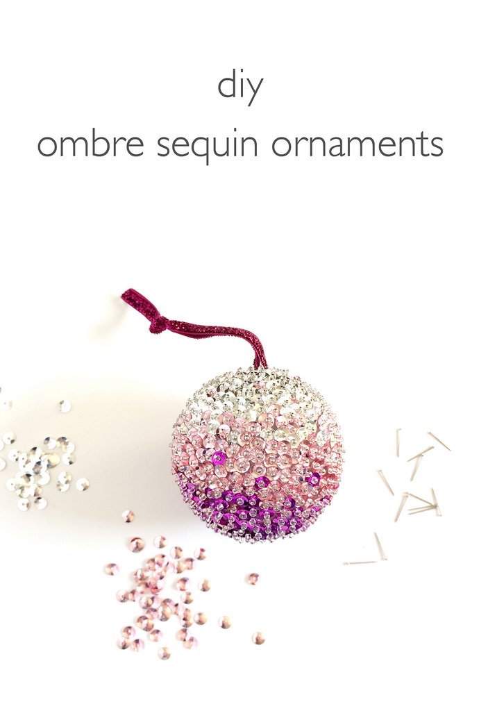 Glamorous holiday tree featuring gilded champagne glitter ombre glass ornament glowing in warm ambient living room corner light.