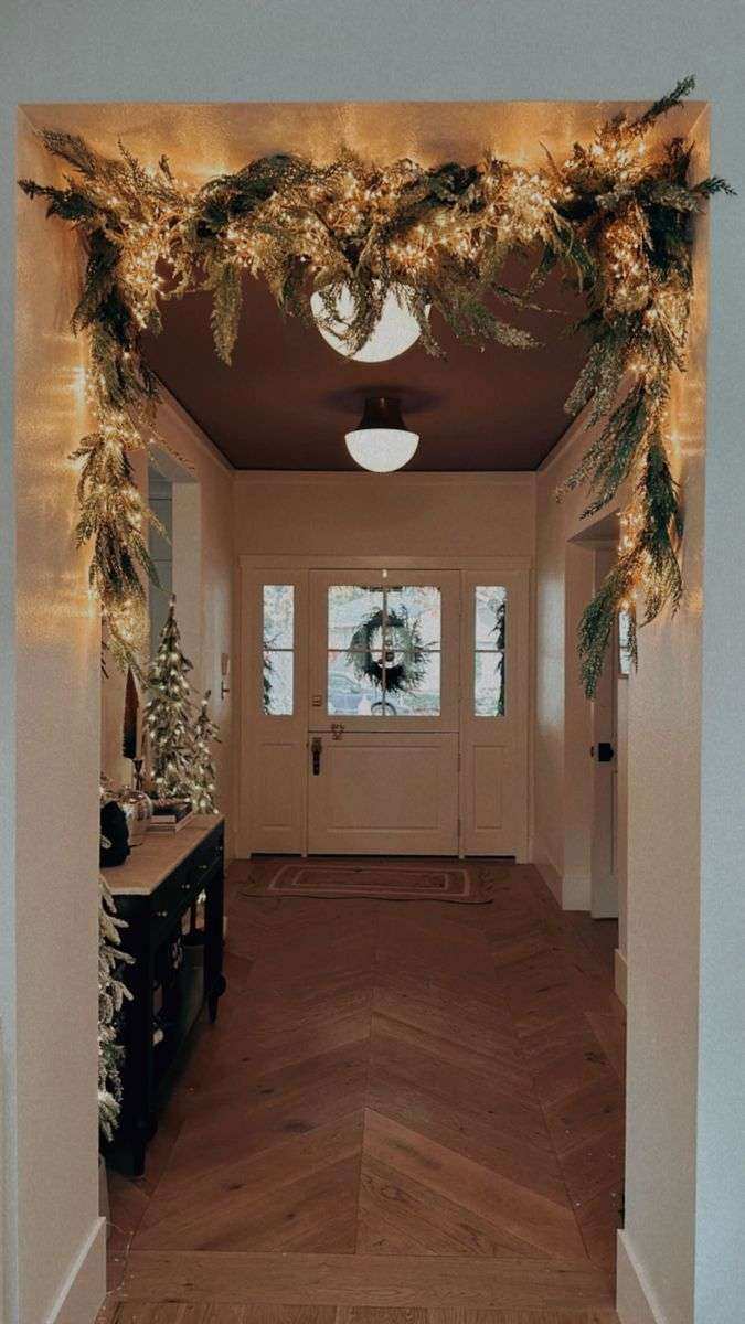Entry doorframe featuring a garland lit with warm white fairy lights, accented by gold pinecones.