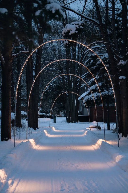 Cobblestone driveway framed by overhead illuminated iron light arches, white twinkle lights, winter foliage.