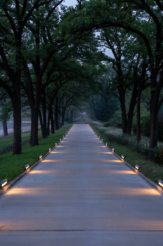 Clean gravel driveway bordered by modern ground stake warm LED lights, winter hedges, stone curb.