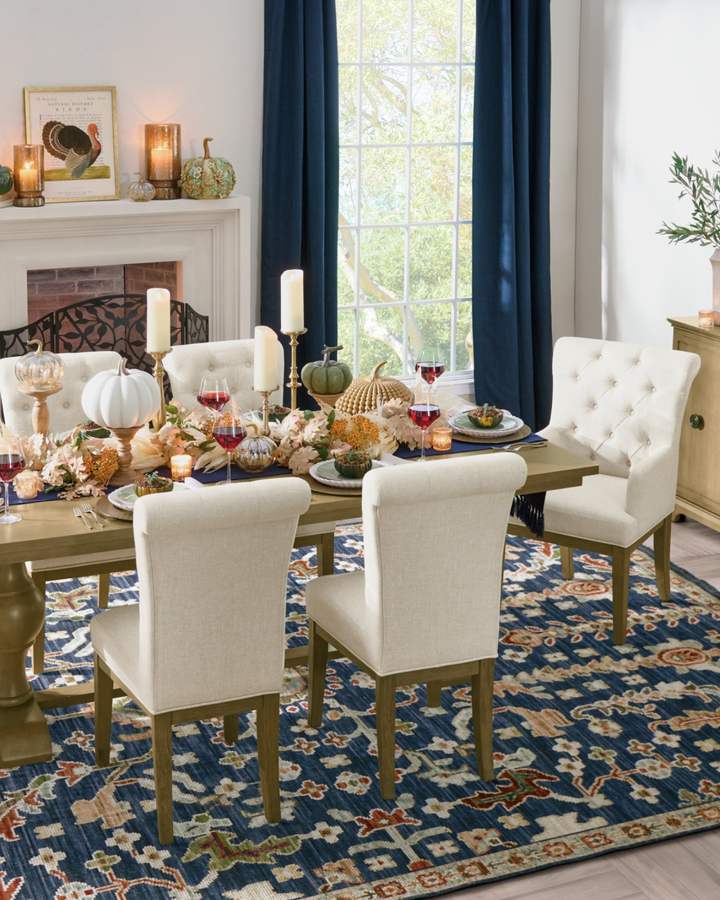 Formal dining room with polished table, elegant pumpkins, tall candles, turkey artwork, mantel display, cool white lighting.