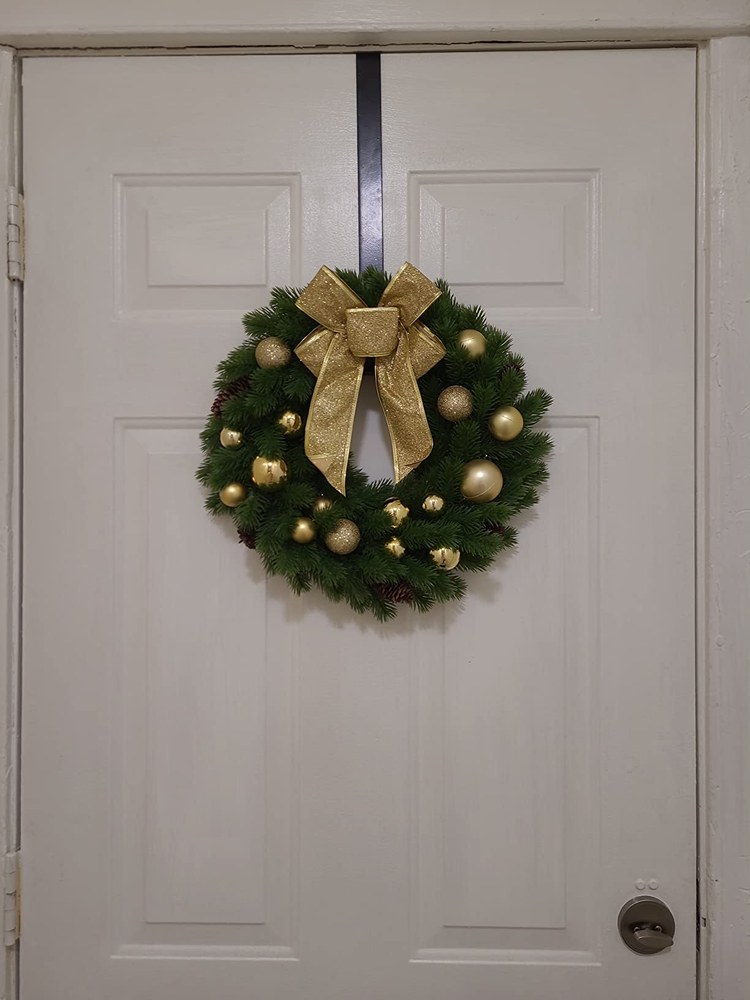 Luxury front entrance showcasing gold painted leaves and ornaments on pine wreath with warm light.