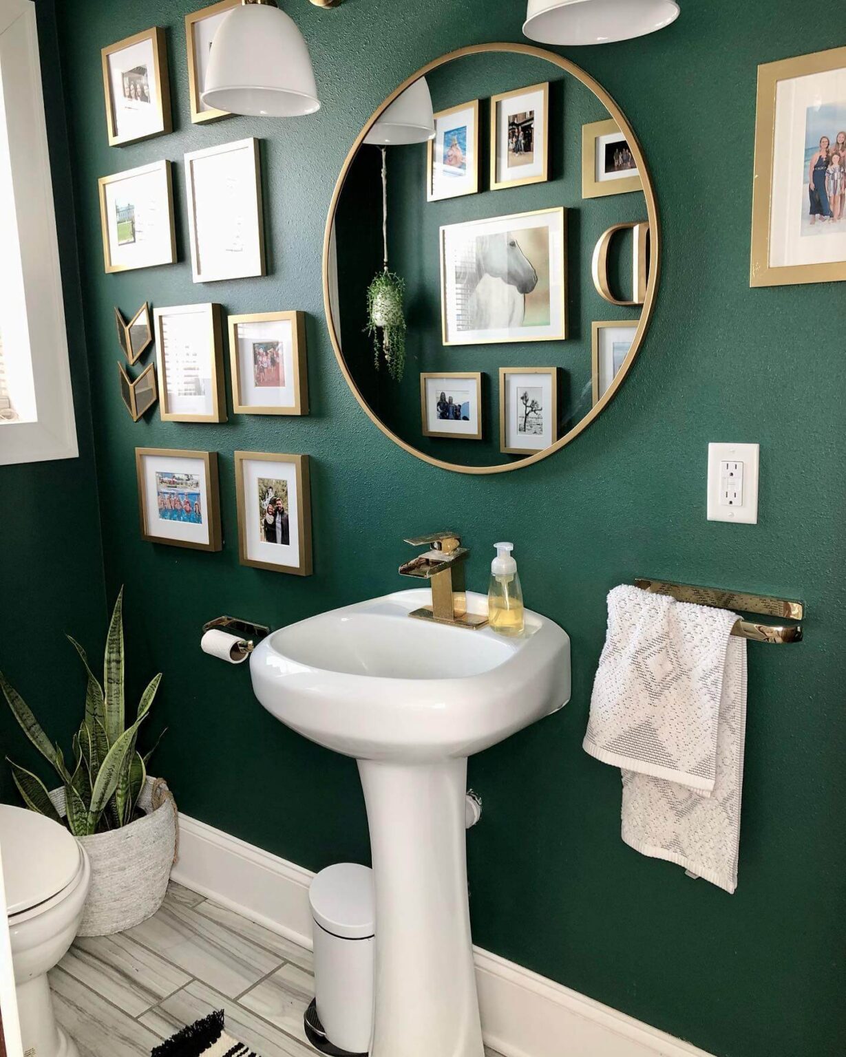 Half bathroom with emerald green walls, gold picture frames, sleek white sink.