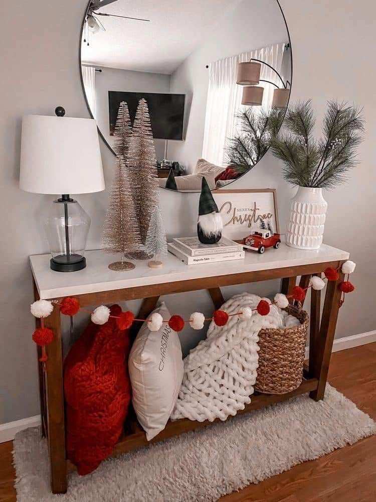 Entryway console table adorned with a small pine garland, red candles, and a decorative vintage metal sled.
