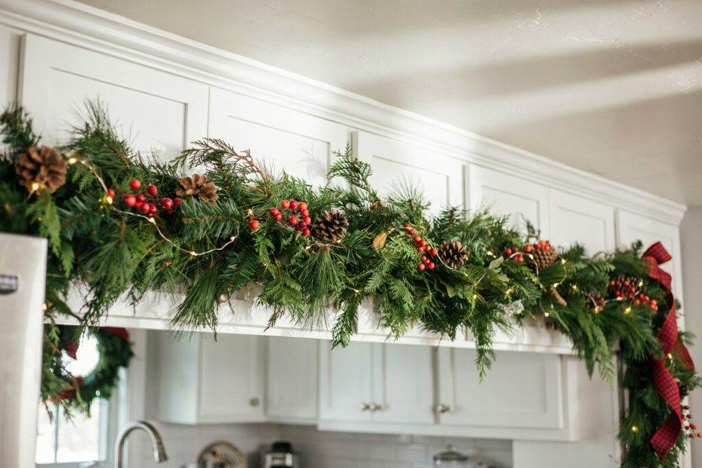Shaker cabinets with simple boxwood wreaths, silk ribbons, cream paint, bright kitchen lighting.