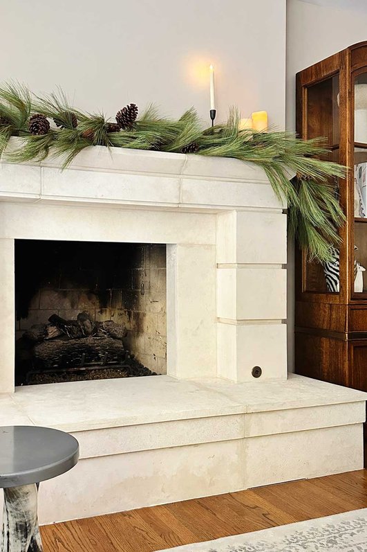 Transitional living room displaying ultra-full faux garland, stone fireplace, modern art, and warm recessed lights.