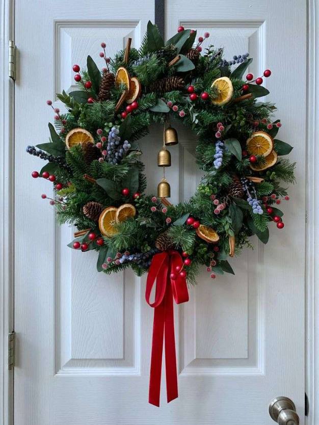 Front door featuring a large circular wreath of mixed evergreen branches, red berries, and a velvet red bow.