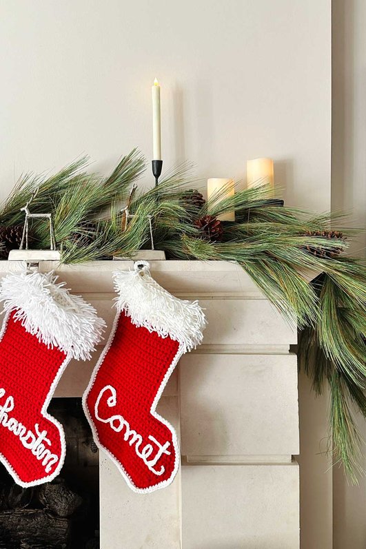 Living room stone fireplace mantel draped in cedar garland with knit stockings and warm lighting