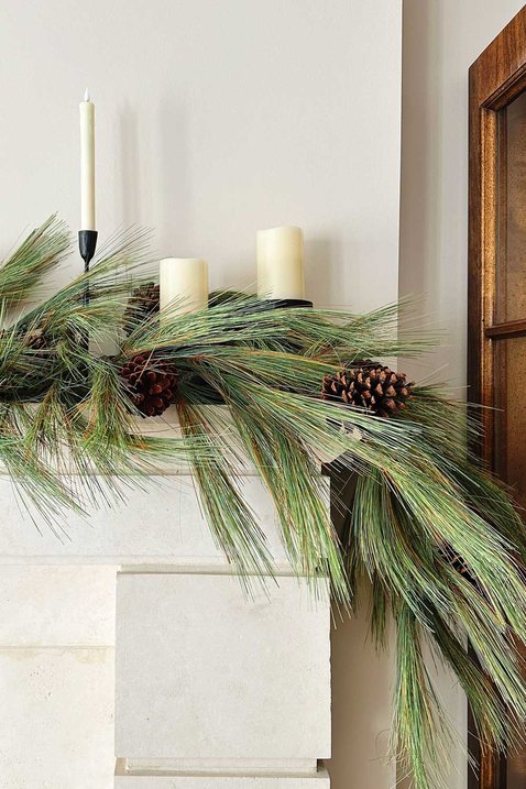 Traditional living room fireplace with lush pine garland flanked by glowing white flameless pillar candles