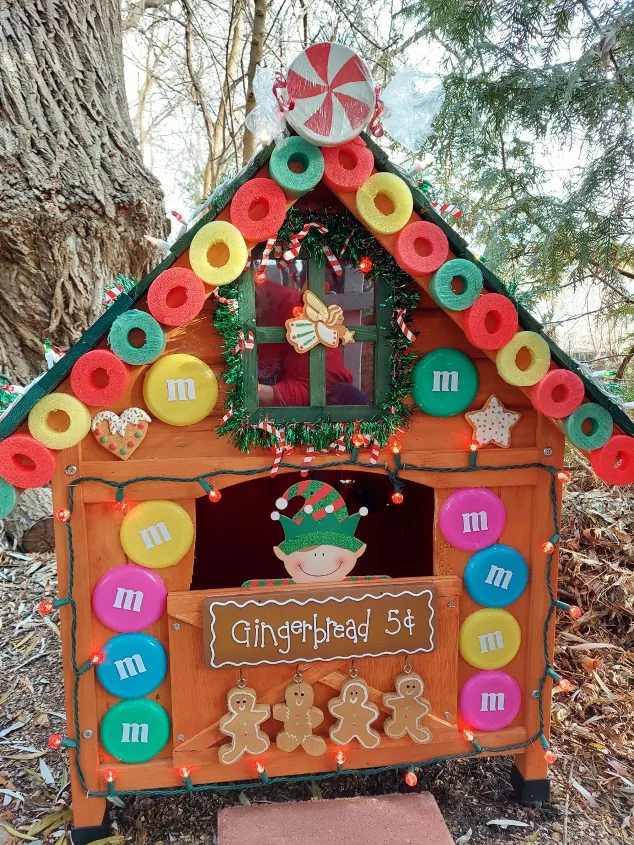 A dog house decorated as a gingerbread house with candy-like outdoor christmas decorations.