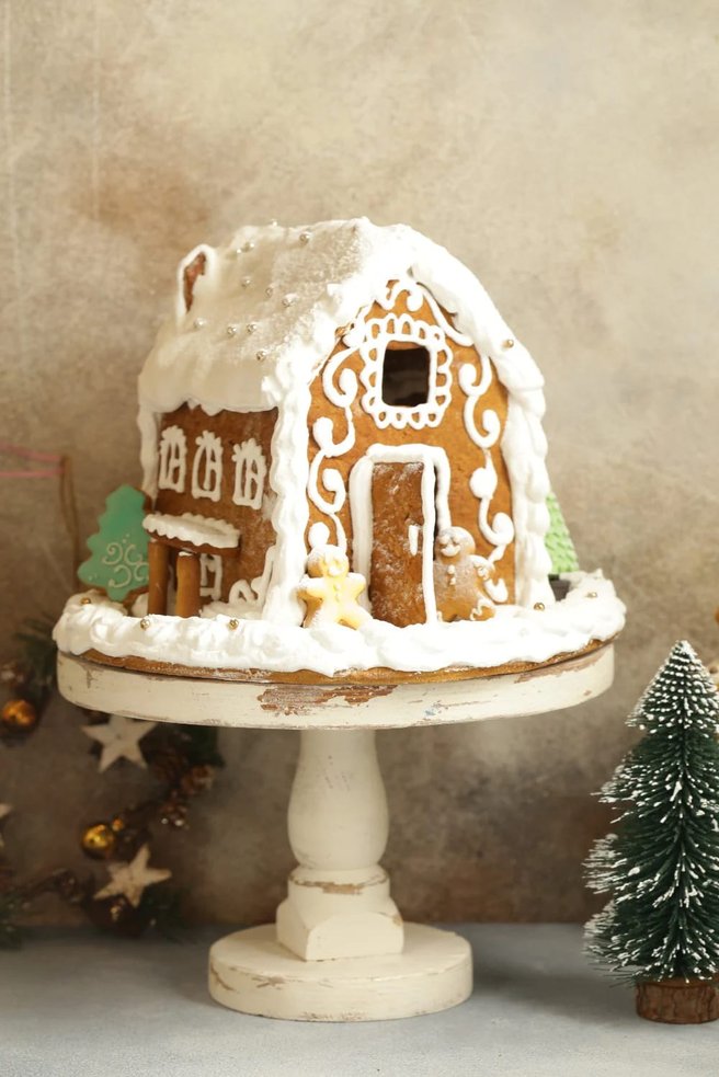 White ceramic cake stand displaying a detailed gingerbread house with candy decorations.