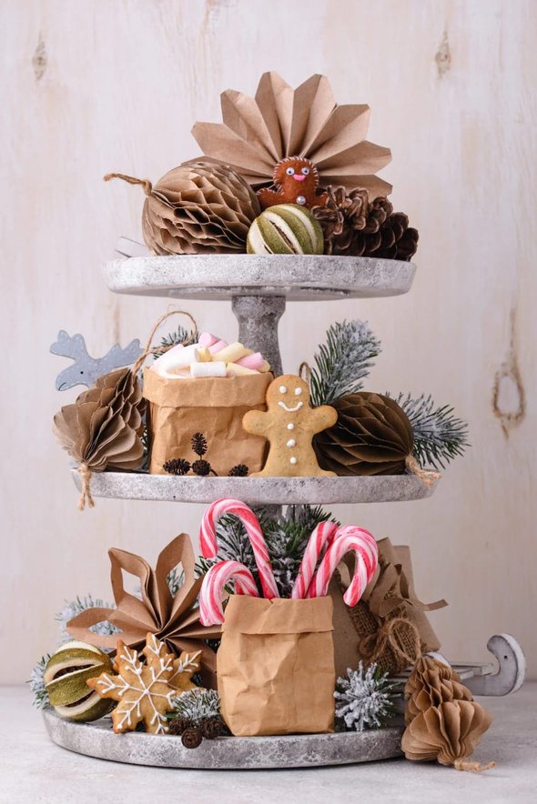 Tiered tray holding gingerbread cookies and small ornaments on the counter.