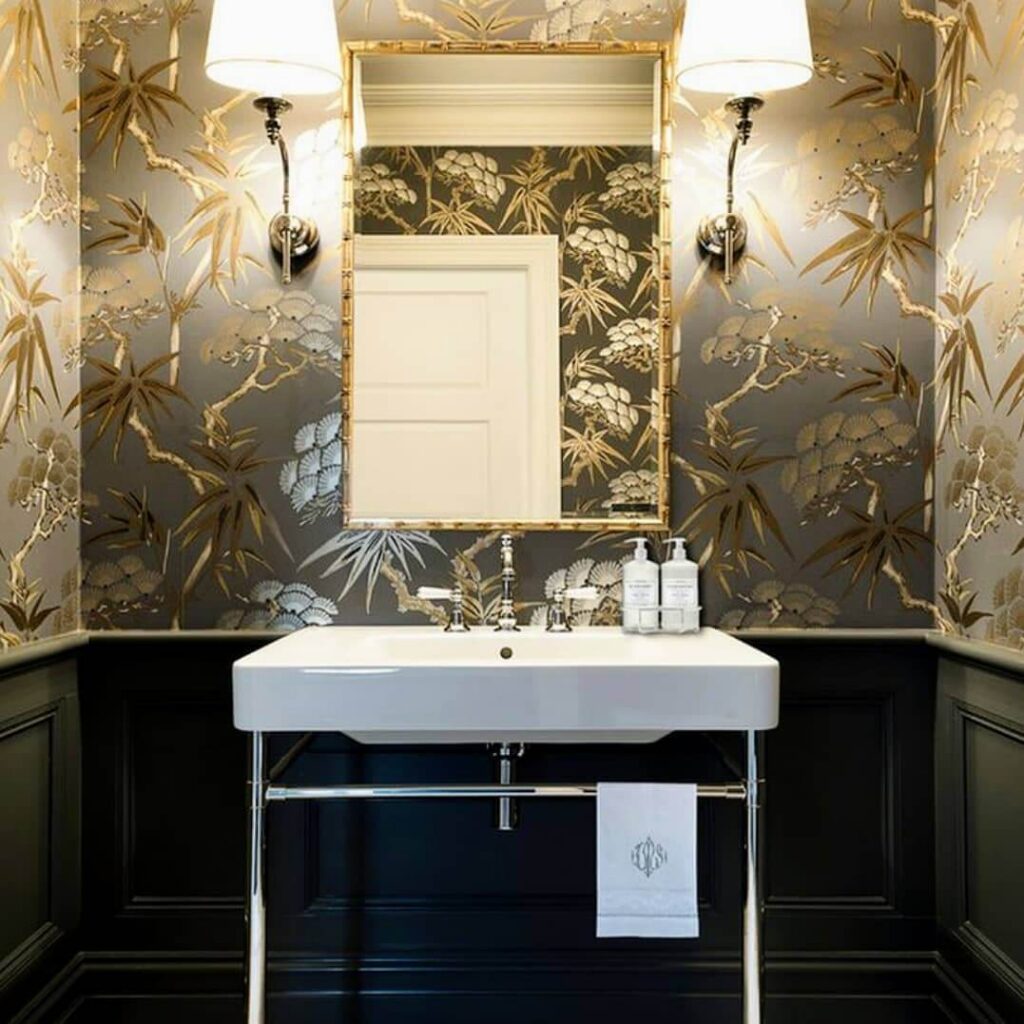 Half bathroom featuring gold botanical wallpaper, console sink, sleek black fixtures.