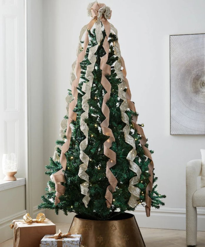 High-ceiling living room tree with oversized gold bow topper, velvet armchair, chandelier lighting