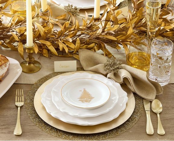Festive dining room table displaying shimmering gold leaf garland over crisp neutral linen runner under lighting