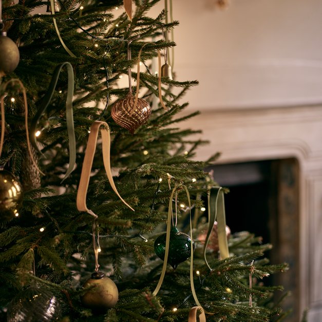Detail shot of Christmas tree with sage velvet and gold metallic ribbons, warm branch lighting