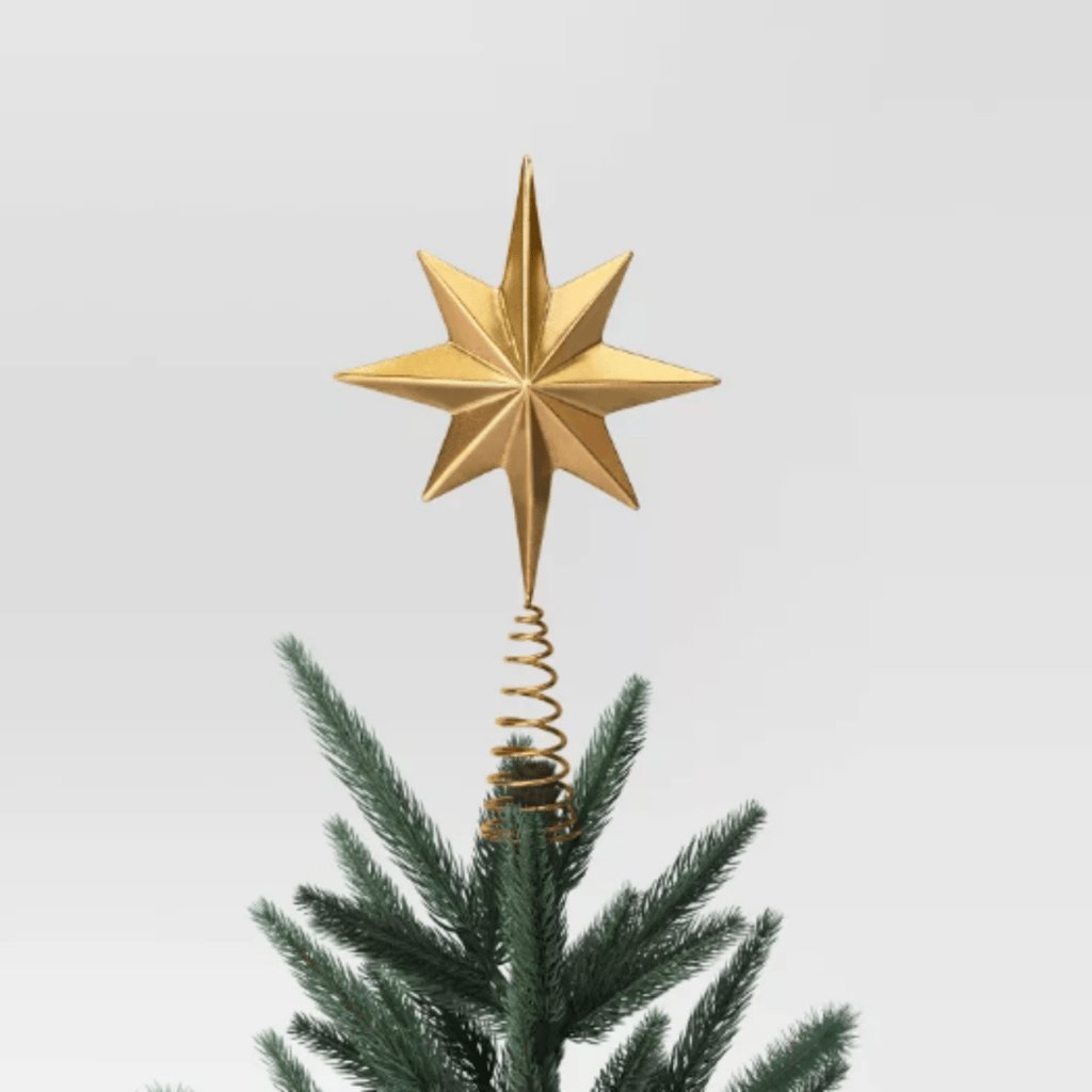 Large gold star tree topper with a textured surface on the peak of a flocked christmas tree.