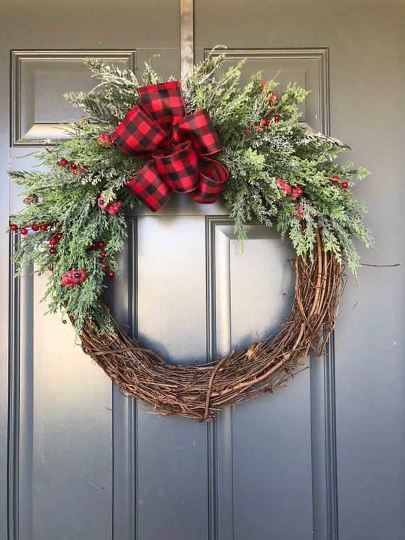 Rustic porch door adorned with dark grapevine wreath featuring tartan plaid ribbon and pine sprigs.