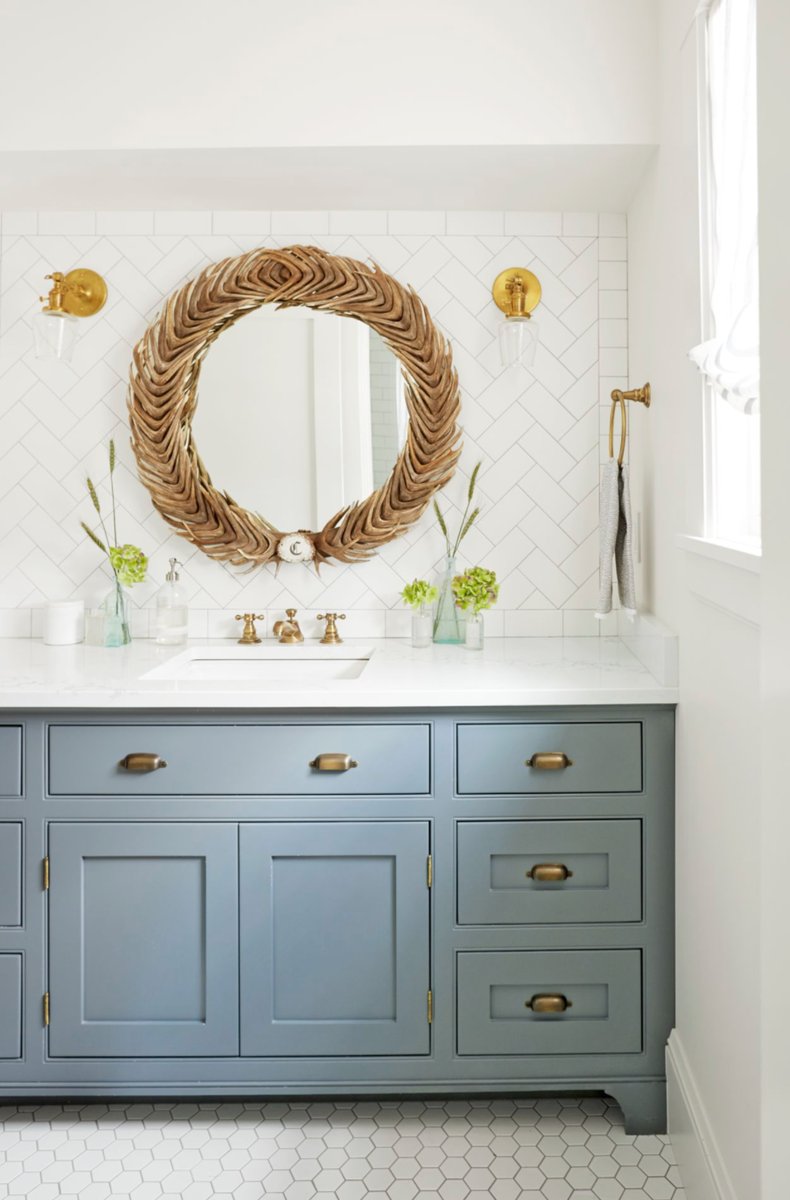 Gray blue vanity with a natural woven rattan mirror and brass accents in a coastal bathroom.