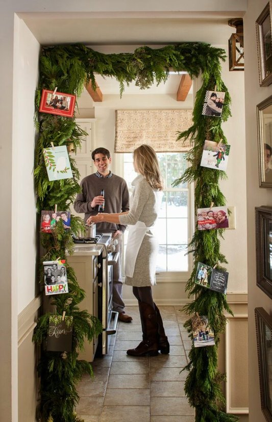 Symmetrical pine garland surrounding interior front door displaying colorful holiday cards with ribbon