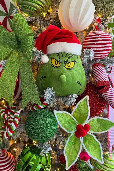 Close up of a green plush Grinch face ornament on a tree branch