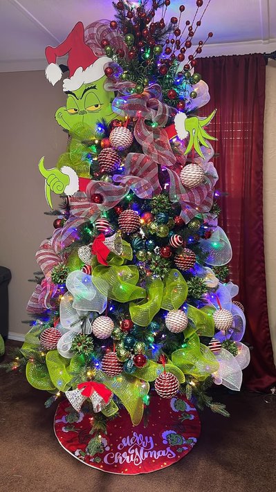 Grinch themed tree beside a white fireplace mantle with green and red decor