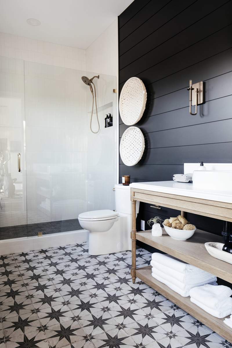 Guest bathroom design with moody black shiplap walls, patterned floor tiles, and soft warm wall sconces.