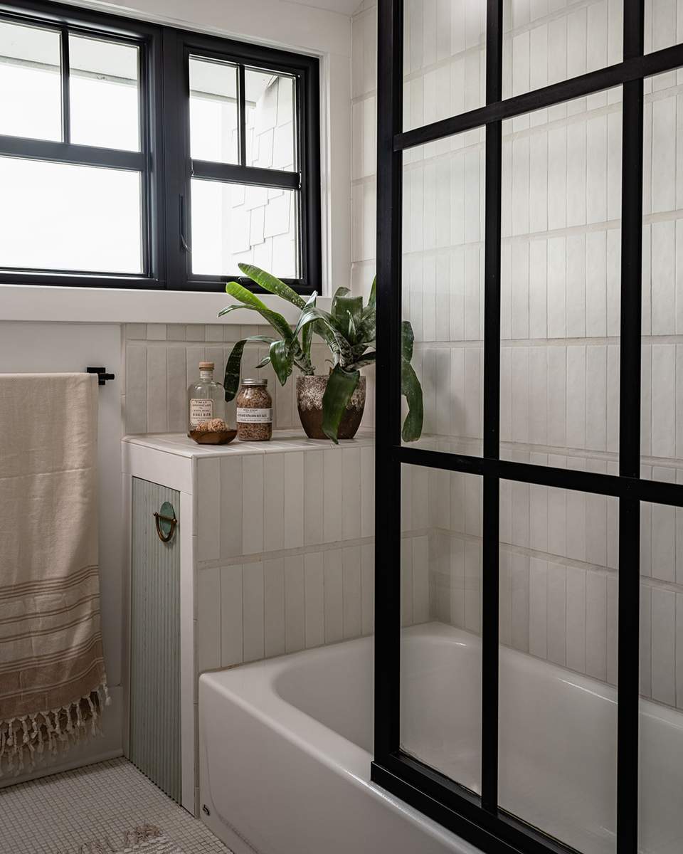Modern guest bathroom showcasing a matte black shower tub enclosure, marble tiles, and dimmable brass lighting.