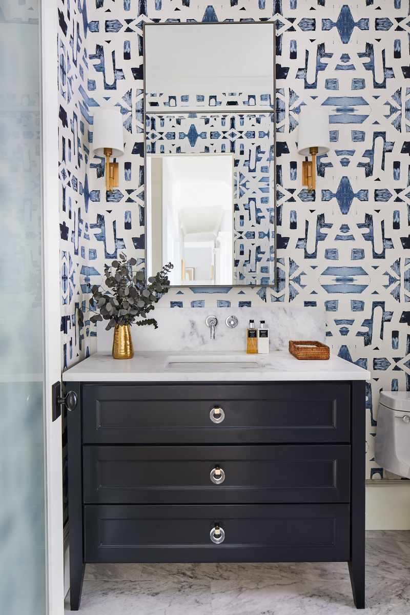 Guest bathroom featuring dark navy botanical wallpaper, black wooden vanity, gold hardware, and soft warm lighting.