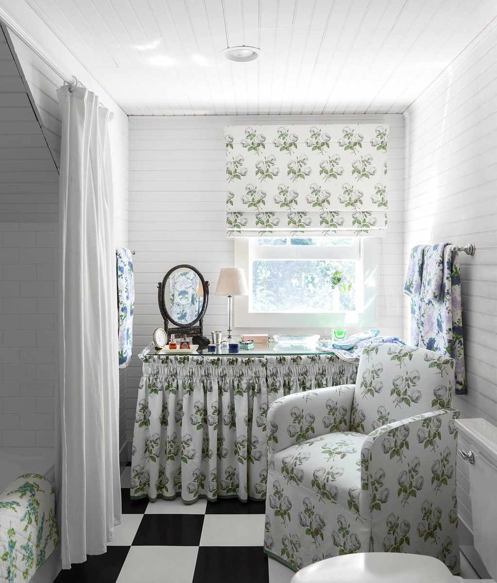 Guest bathroom featuring floral print upholstered chair, classic black and white checkered floor, and warm ambient lamps.