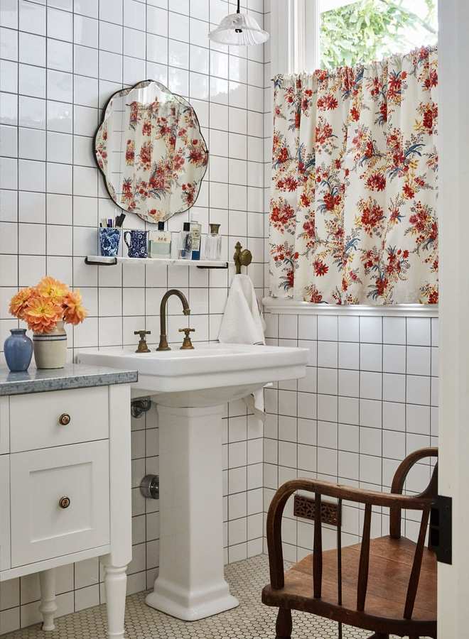 Guest bathroom with white porcelain pedestal sink, romantic floral shower curtain, brass plumbing, and warm lighting.