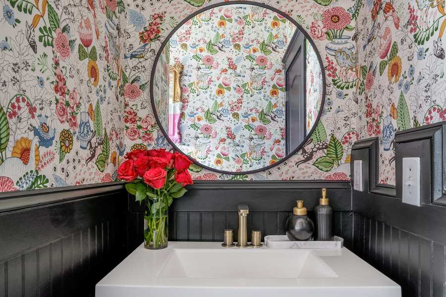 Guest bathroom with dark floral wallpaper, black trim, matte black vanity, and warm glowing wall sconces.