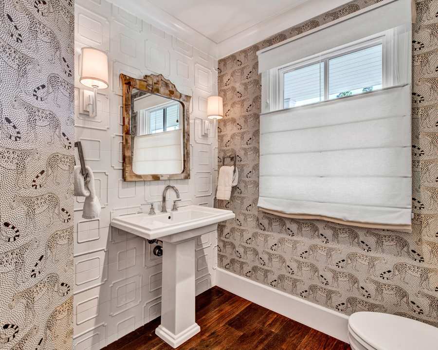 Guest bathroom featuring whimsical floral wallpaper, white porcelain pedestal sink, and warm golden wall sconce lighting.