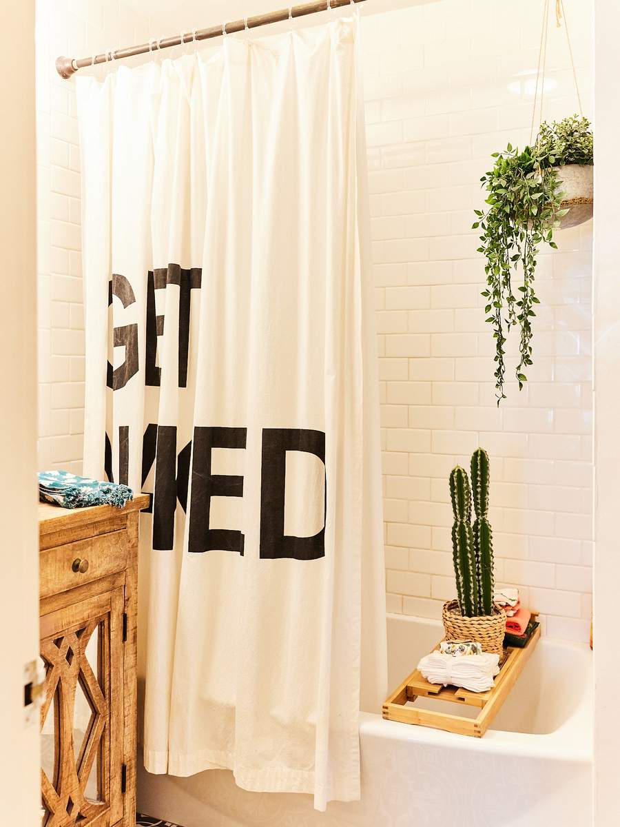Guest bathroom design featuring bold graphic shower curtain, crisp white tile, and warm Edison pendant lighting.