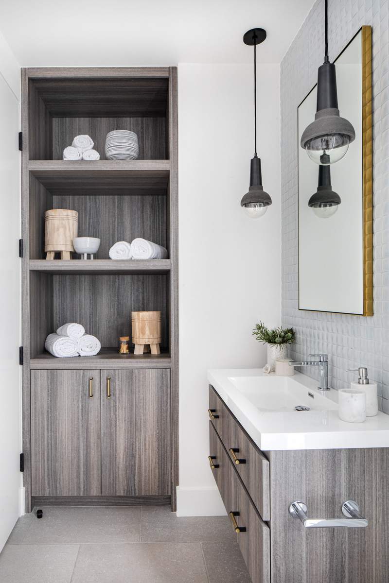 Guest bathroom design featuring soft gray vanity with open lower shelving, stacked towels, and warm vanity lighting.