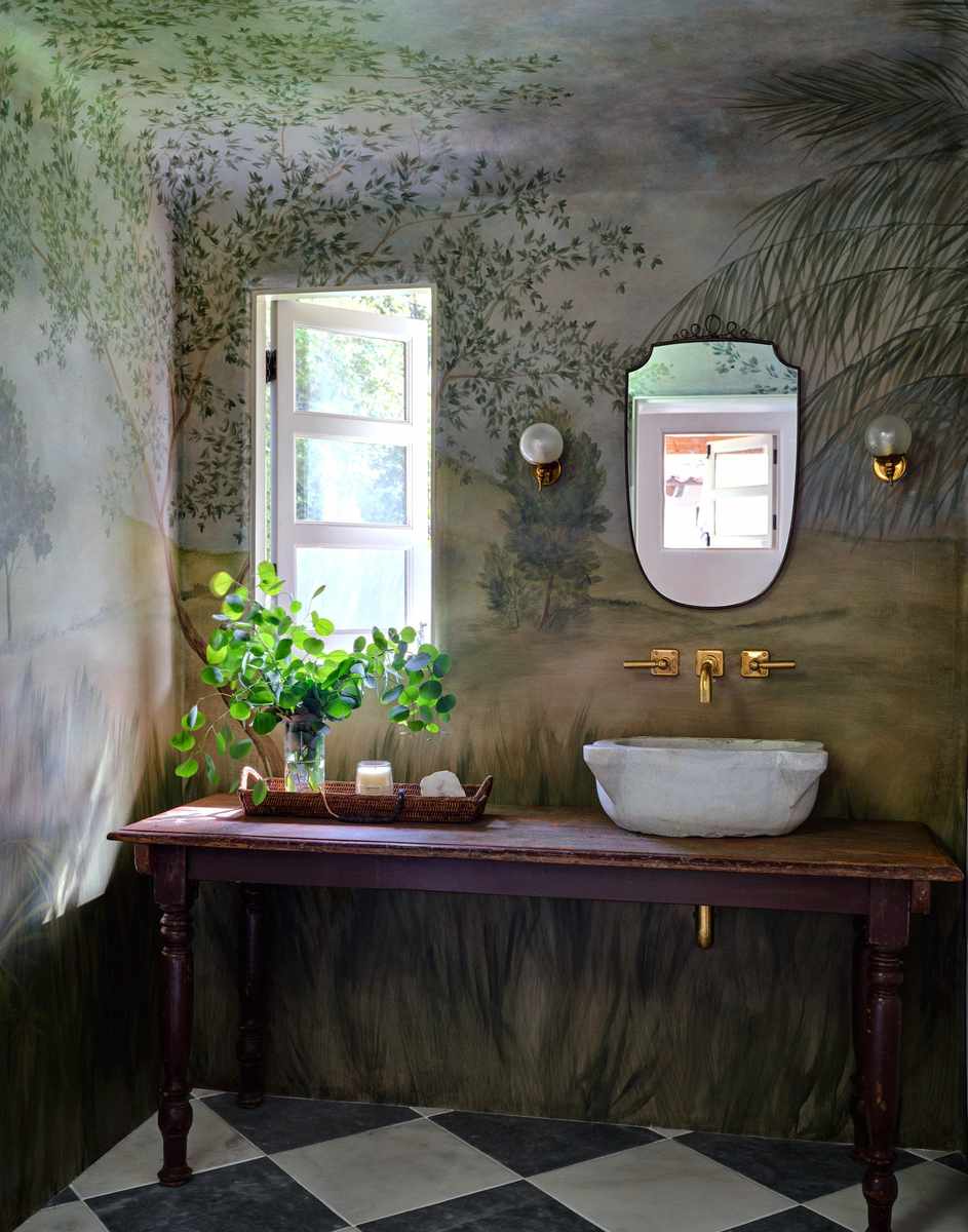 Guest bathroom featuring lush green nature wall mural, ceramic vessel sink on raw wood vanity, and soft warm lighting.