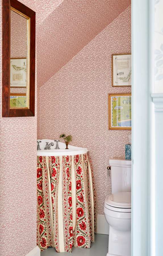 Feminine guest bathroom with floral pink wallpaper and a charming fabric skirted sink vanity.