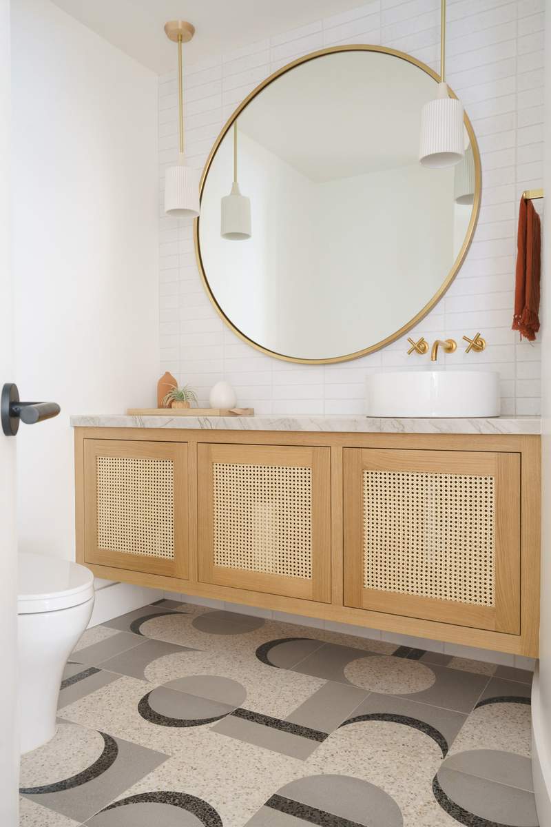 Boho-inspired guest bathroom with a natural rattan vanity and a large circular mirror.