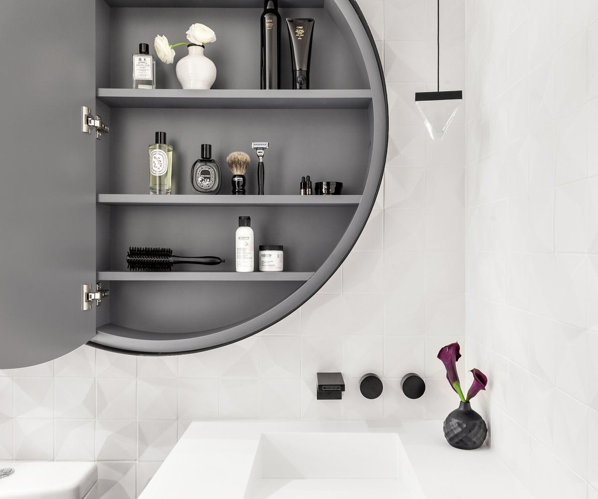 Minimalist guest bathroom featuring a round mirror hung above a functional wall-mounted cabinet.