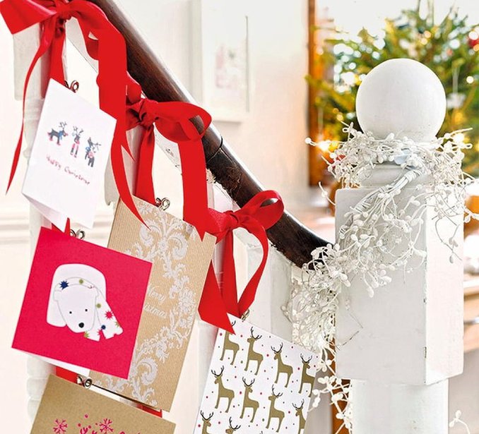 Traditional staircase banister draped in pine garland with red velvet ribbons holding holiday cards